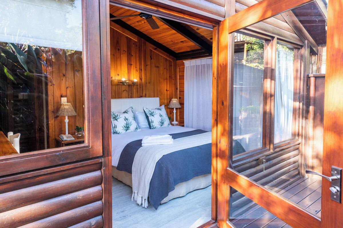 Ein Schlafzimmer einer Holzhütte mit Bett, Nachttischlampen und einem Fenster.