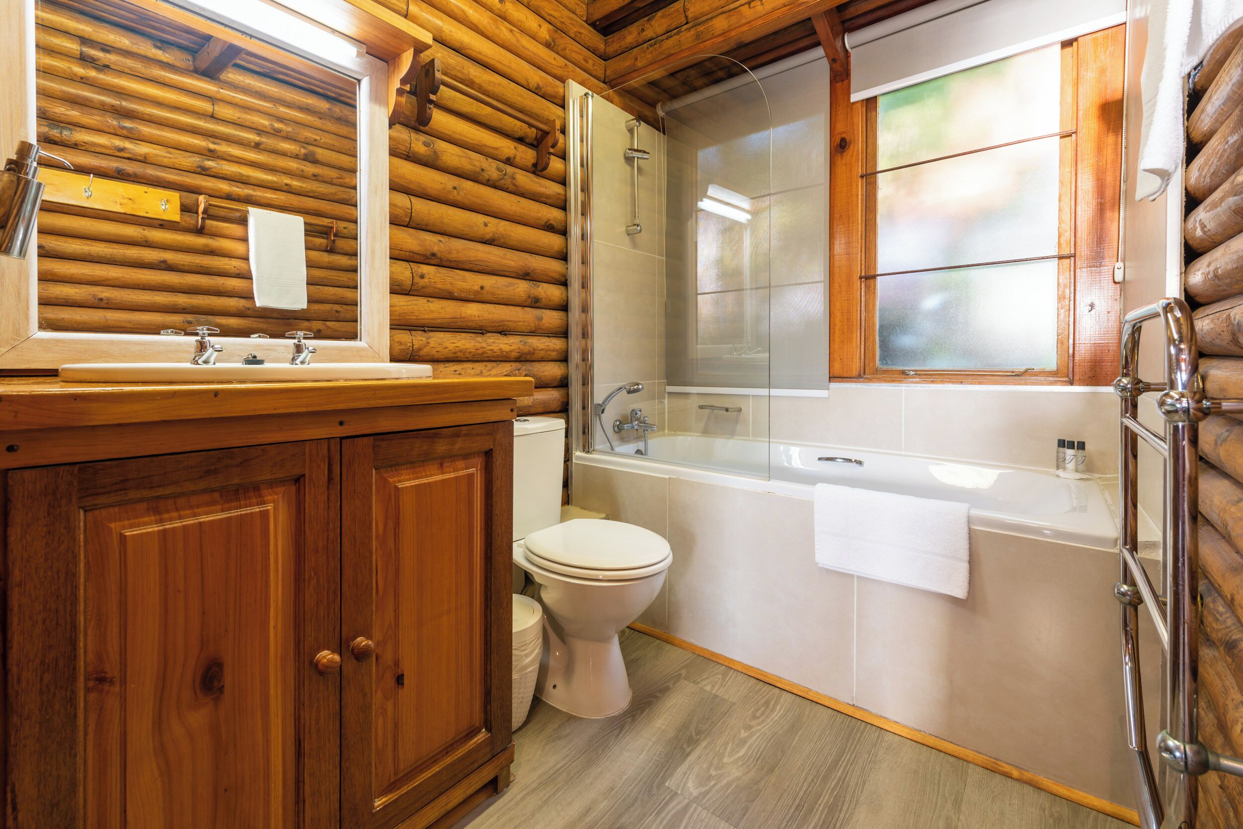 A wooden cabin bathroom with a wooden vanity, a toilet, a bathtub, and a shower.