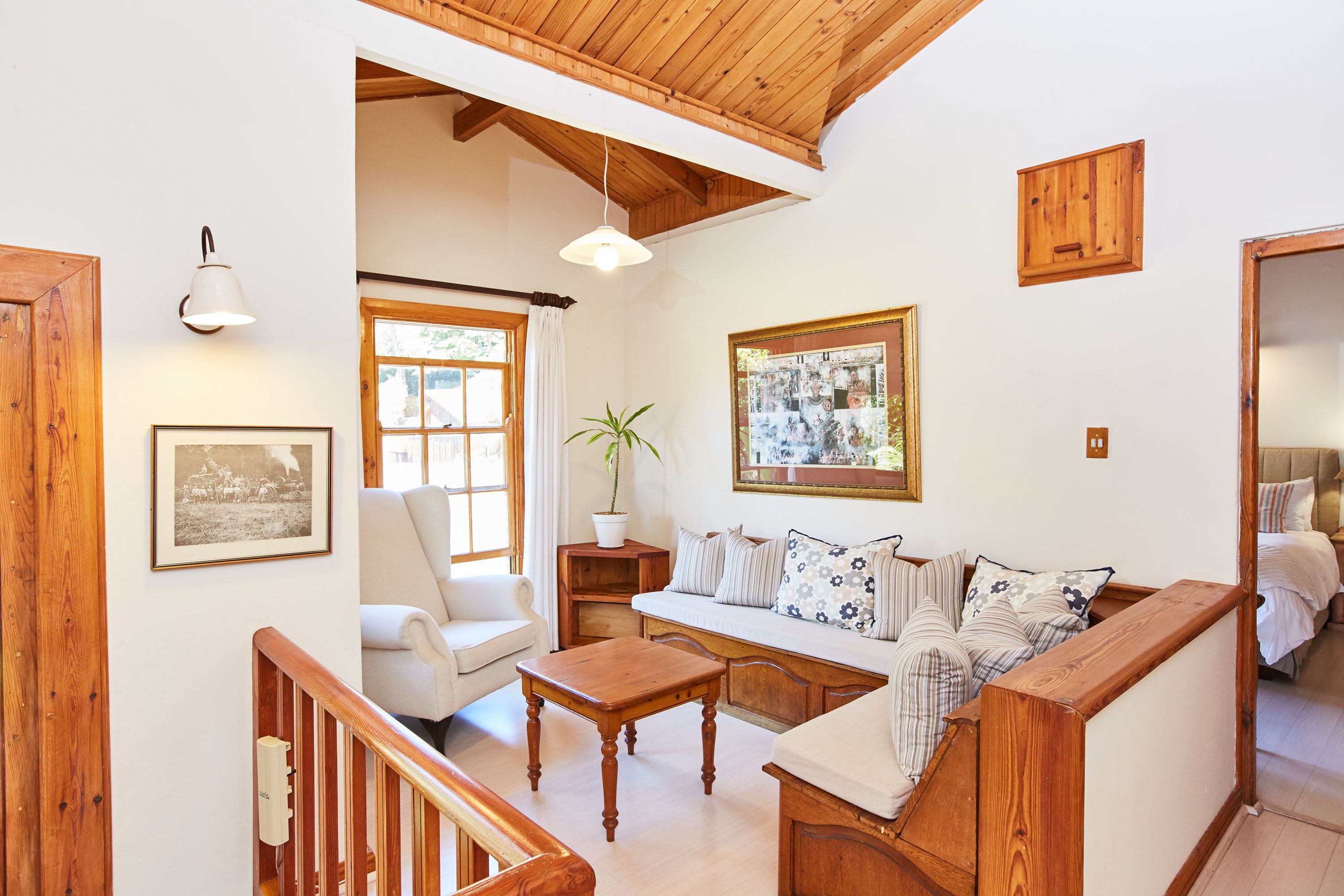 A cozy living room with a wooden bench, a white sofa, and a wooden coffee table. There is a potted plant and a framed picture on the wall.