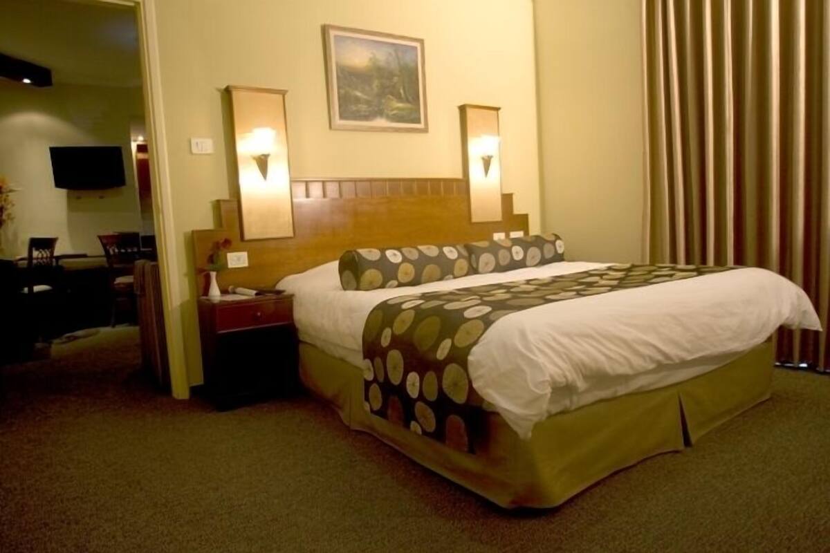 A hotel room with a bed, nightstands, a TV, and a painting on the wall.