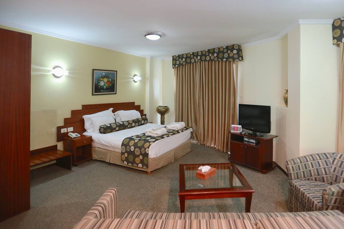 A hotel room with a bed, a television, a sofa, a coffee table, and curtains.