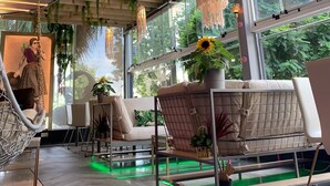 A modern interior with hanging plants, a hammock, and a view of greenery outside. - Royal Court Hotel (Ramallah)