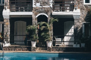 Un bâtiment en pierre doté d’une piscine, caractérisé par une façade en pierre, des portes en arc de cercle et des plantes en pot.