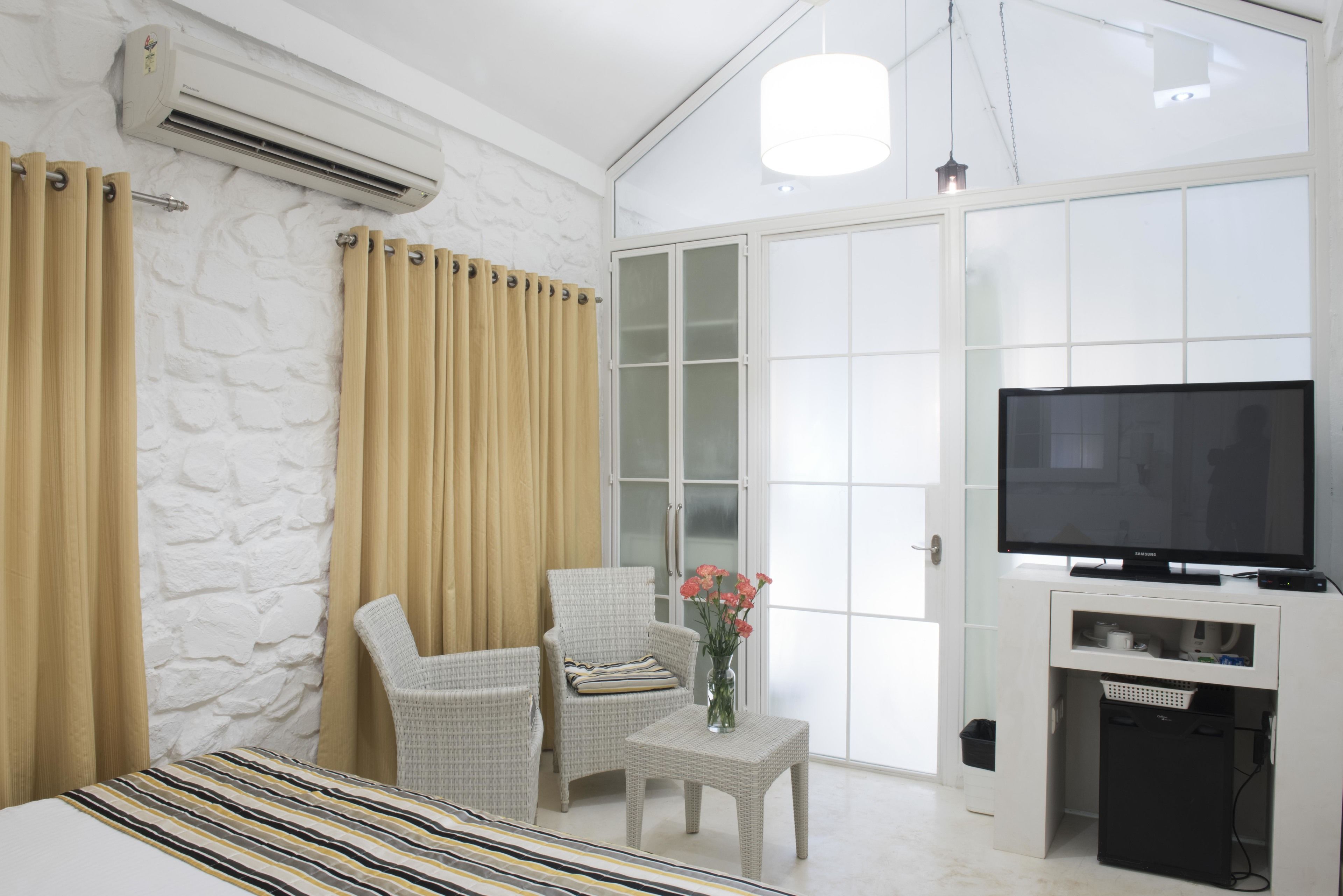 A hotel room with a bed, a chair, a small table with a vase, a TV, and a white wardrobe.