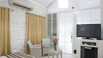 A hotel room with a bed, a chair, a small table with a vase, a TV, and a white wardrobe.