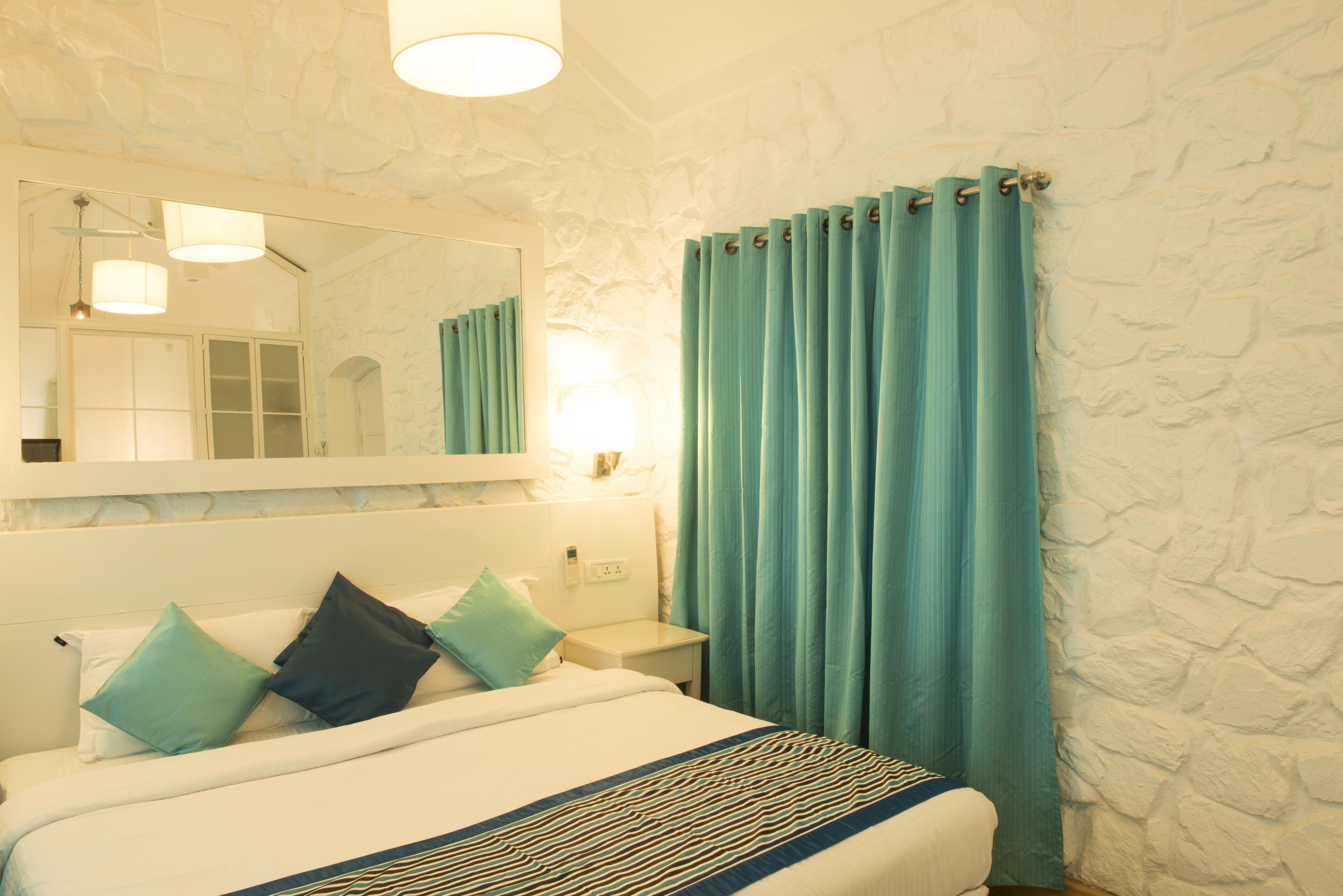 Une chambre d’hôtel avec un lit, une table de chevet, un miroir et une fenêtre avec des rideaux.
