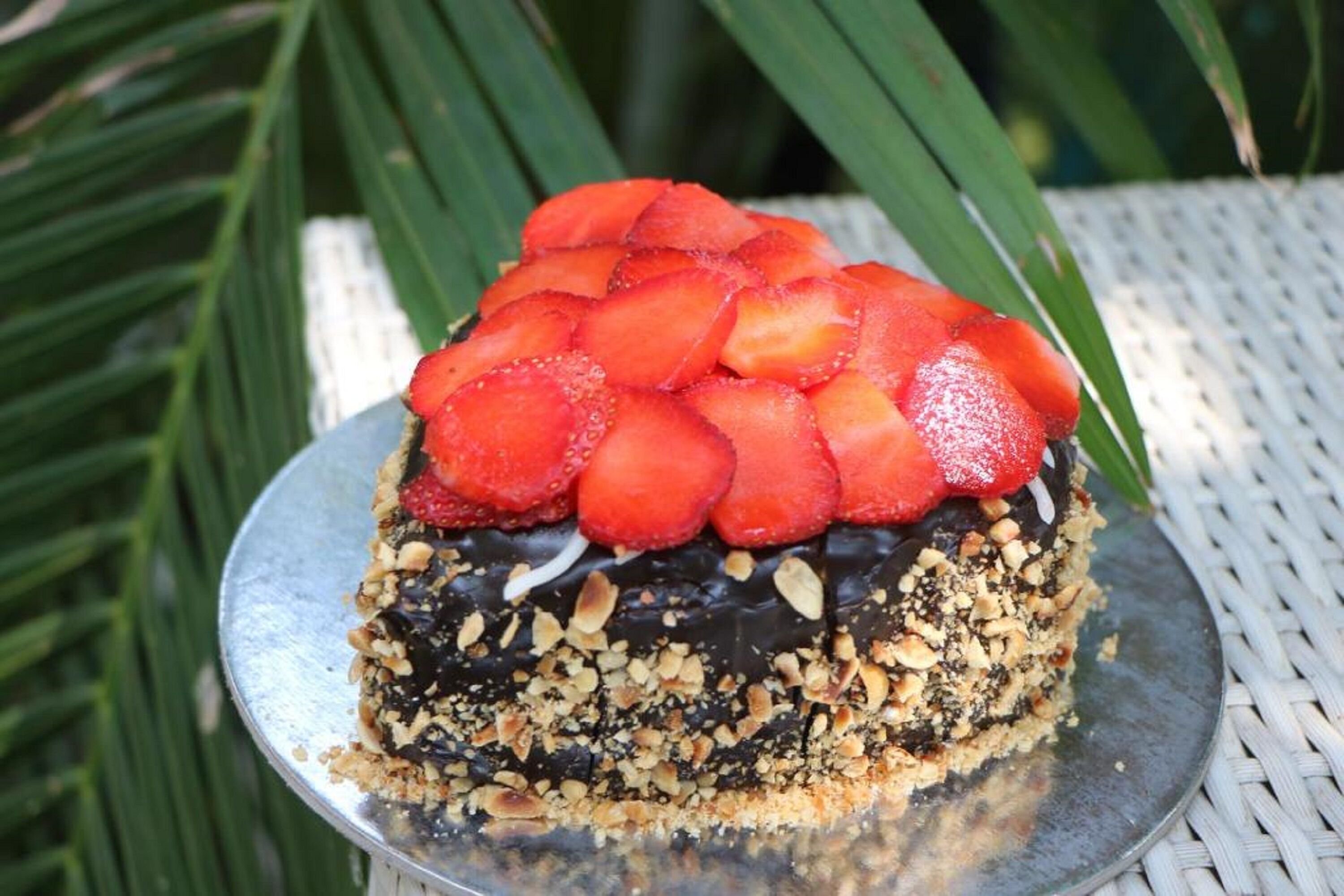 A dessert on a metal plate with a chocolate base, topped with strawberries and crushed nuts.