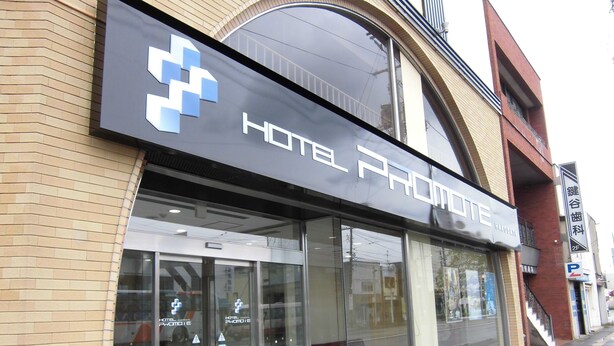 A hotel entrance with a glass door, a sign above the door, and a brick building facade. - Hotel Promote Hakodate (Hakodate)