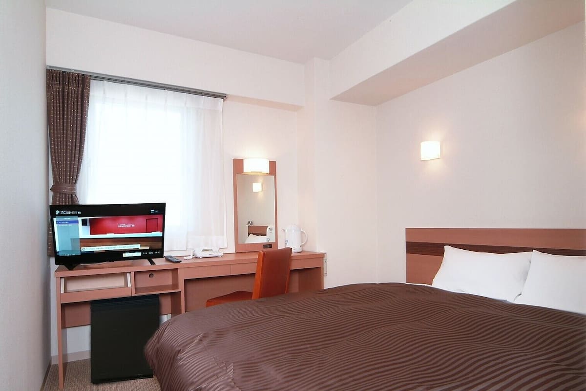 A hotel room with a bed, desk, chair, television, and a mirror.