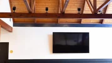 A room with a wooden ceiling, a flat-screen TV mounted on the wall, and a seating area with leather sofas and a small round table.