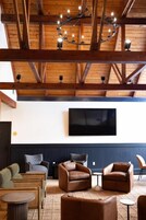 Una habitación con techo de madera, televisor de pantalla plana en la pared y zona de estar con sofás de cuero y una pequeña mesa redonda.