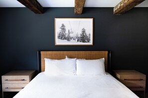 Une chambre à coucher avec un lit, deux tables de chevet, un tableau encadré au mur et des poutres apparentes.