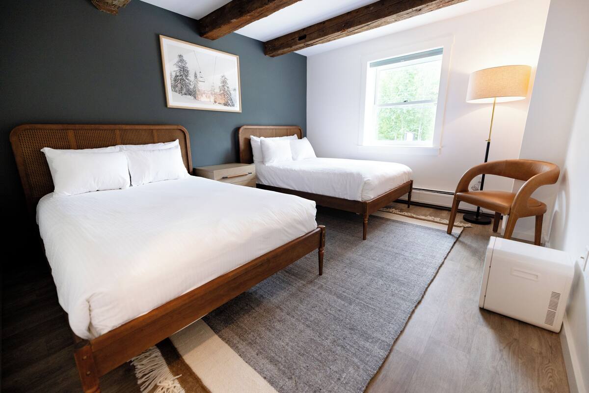 A bedroom with two wooden beds, a chair, a lamp, and a radiator.