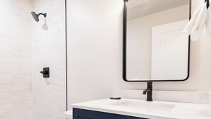 Un baño moderno con inodoro blanco, tocador azul oscuro con detalles dorados y espejo con tres luces.