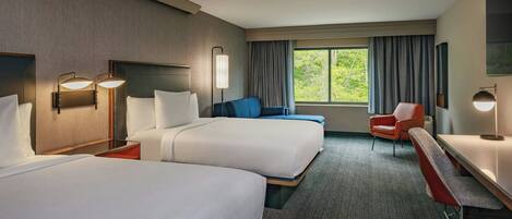 A hotel room with two beds, a desk, a chair, and a large window with curtains.