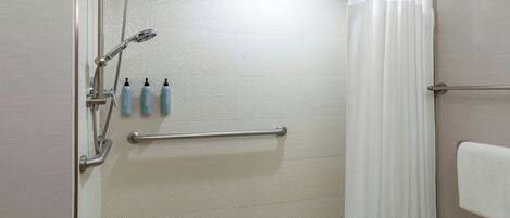 Zona de ducha con cabezal de ducha manual, barra de apoyo y tres botellas de champú.