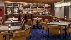 A restaurant with multiple tables and chairs, a bar area with shelves of bottles, and a menu board. - Courtyard Oneonta (Oneonta)
