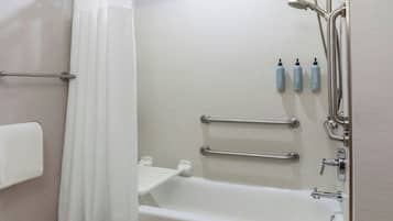 A bathroom with a bathtub, shower, and handrails.