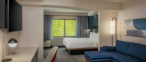 Une chambre d’hôtel avec un lit, un bureau avec une lampe, une chaise, un canapé et un téléviseur fixé au mur.