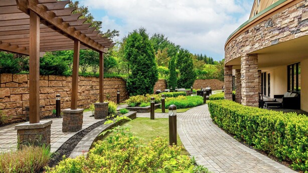 A landscaped outdoor area with a pergola, stone pillars, and a curved pathway. - Courtyard Oneonta (Oneonta)