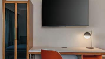 Een hotelkamer met een grote flatscreen televisie aan de muur, een bureau met een lamp en een schuifdeurkast.