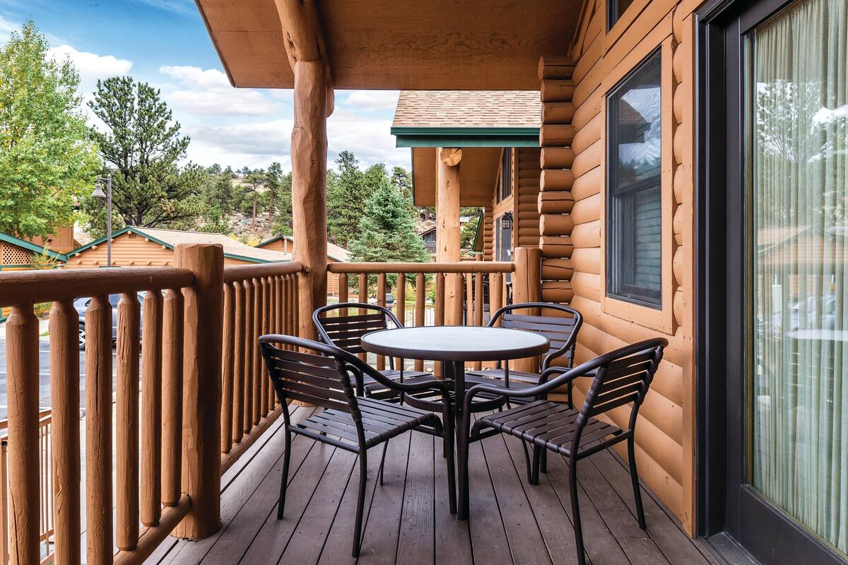 A wooden deck with a round table and four chairs, overlooking a scenic landscape.