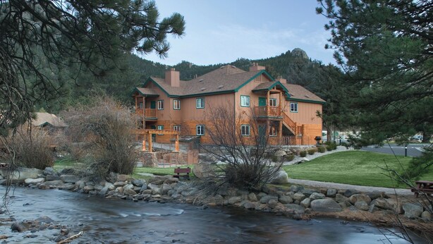 A lodge with a stone retaining wall, a wooden deck, and a view of a river. - WorldMark Estes Park (Estes Park)