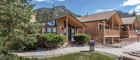 A log cabin-style hotel with a large deck and a mountain backdrop.