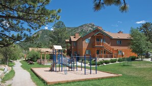 A two-story wooden house with a balcony, surrounded by a grassy area and a playground. - WorldMark Estes Park (Estes Park)