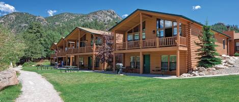 Un hôtel de style chalet en bois, doté de nombreuses chambres, d’un espace extérieur couvert avec des sièges et offrant une vue pittoresque sur les montagnes.