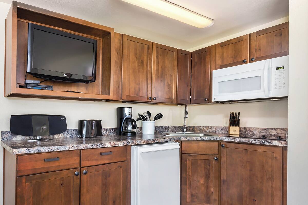 A kitchen with wooden cabinets, a built-in microwave, a coffee maker, and a dishwasher.