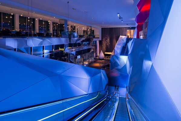 A modern interior with an escalator, glass railings, and a seating area with tables and chairs. - Radisson Blu Mall of America (Bloomington)