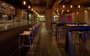 A bar area with wooden beams, bar stools, and a long counter with bottles. - Radisson Blu Mall of America (Bloomington)