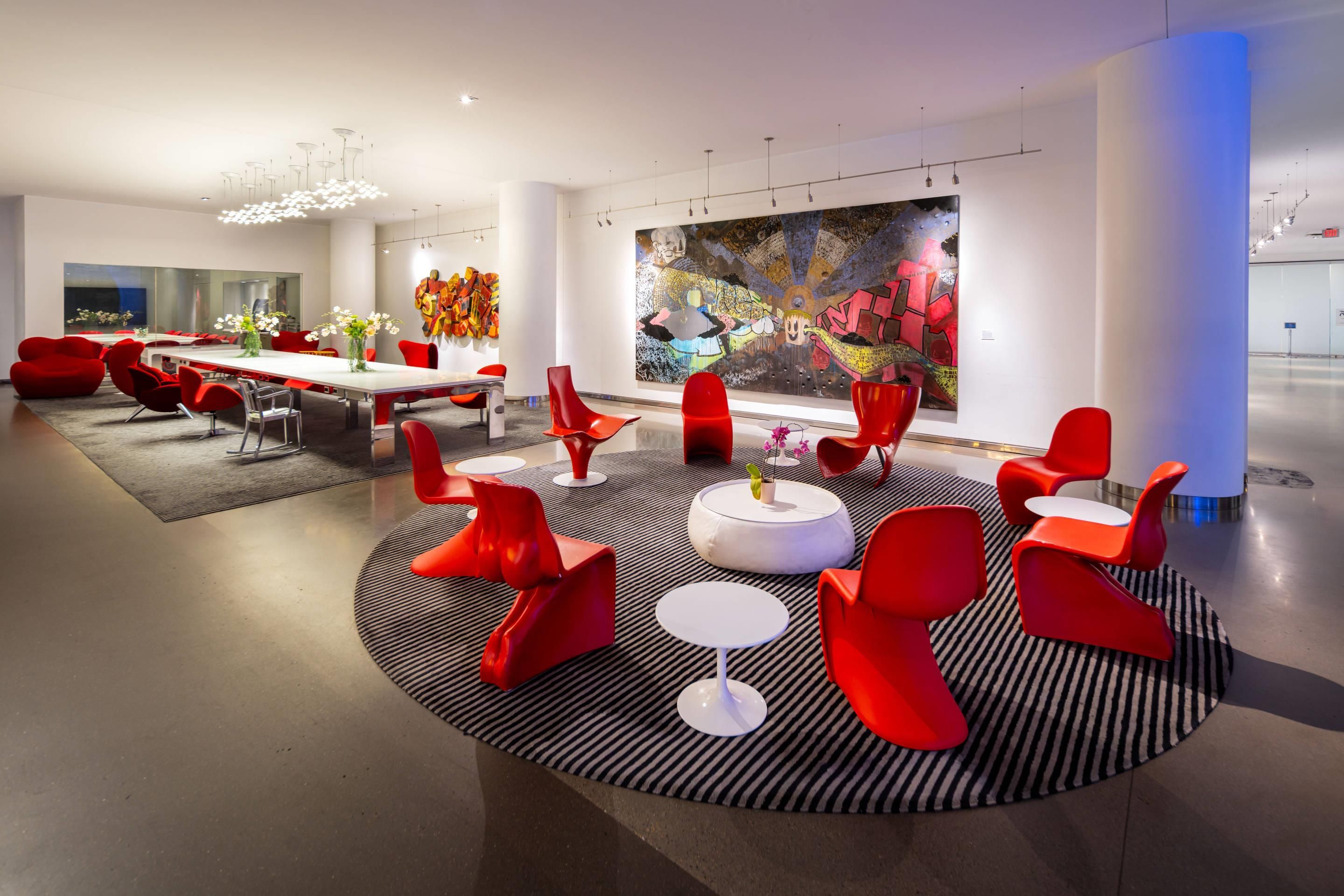 Un espacio lounge moderno con un arreglo central de asientos, una larga mesa de comedor y un gran cuadro abstracto en la pared.