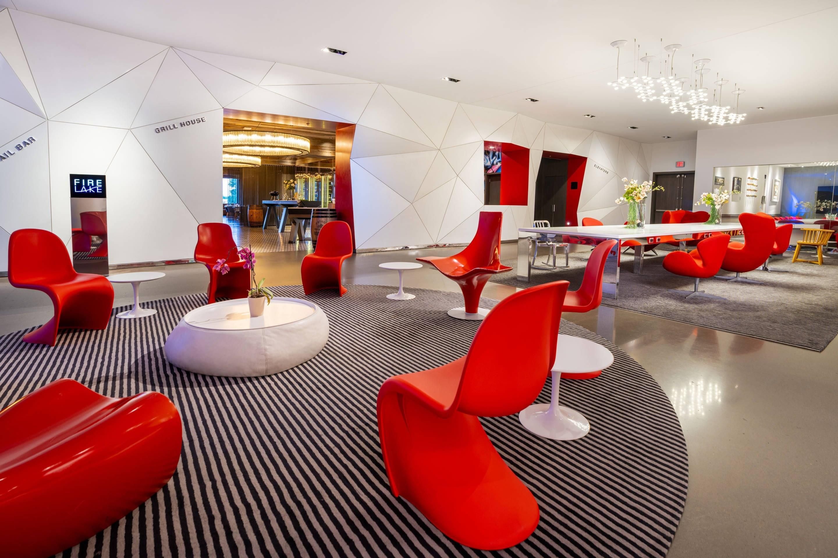 Un espace détente moderne avec des fauteuils rouges, une table ronde blanche et un sol à rayures.