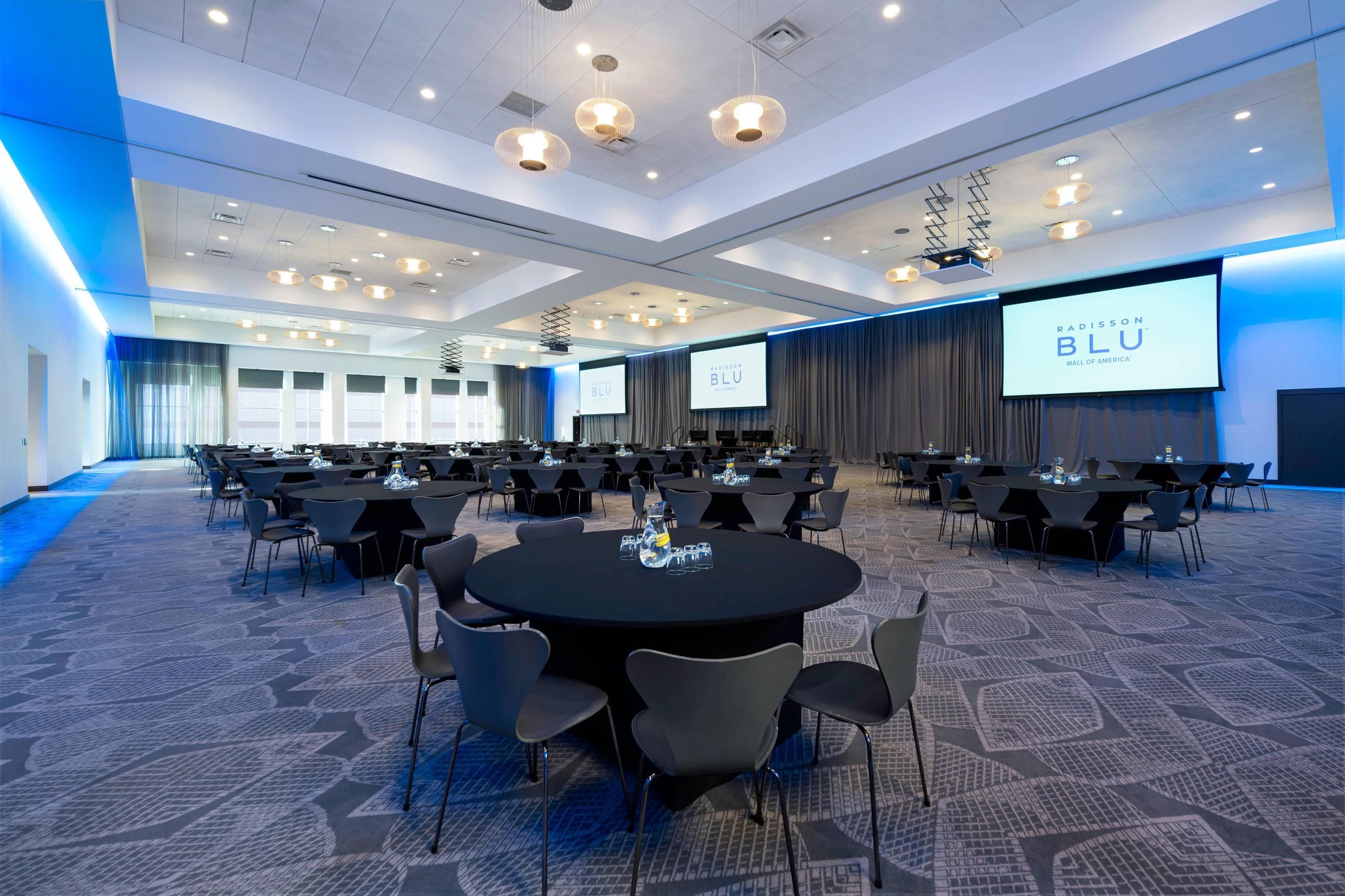 A conference room with round tables, chairs, and a large screen displaying the Radisson Blu logo.