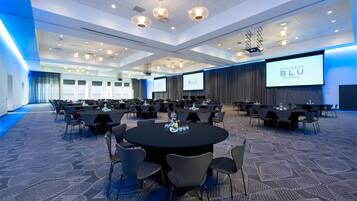 A conference room with round tables, chairs, and a large screen displaying the Radisson Blu logo.