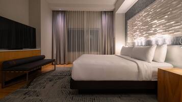 A modern hotel room with a large bed, a bench, a TV, and a decorative wall panel.