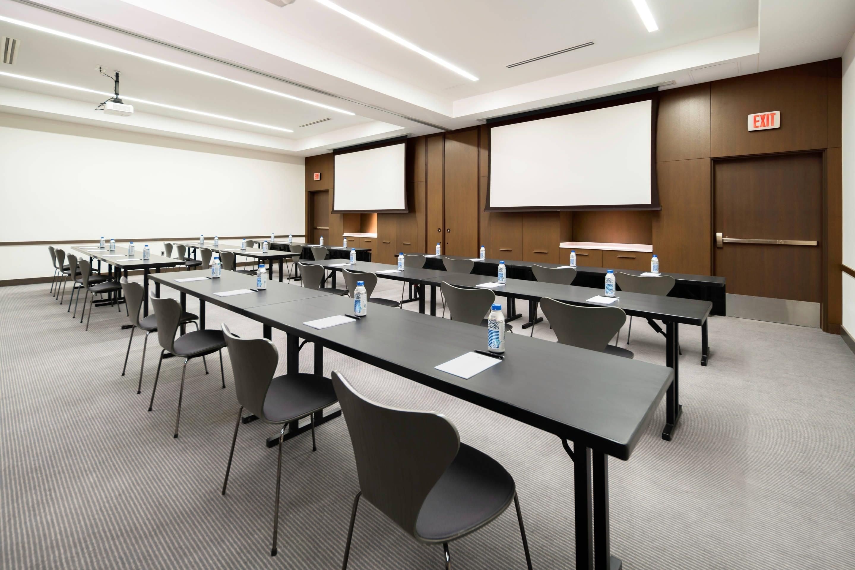 A conference room with long tables, chairs, and a projector screen.