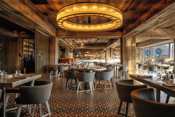 A restaurant with a central bar area, multiple dining tables, and chairs. - Radisson Blu Mall of America (Bloomington)