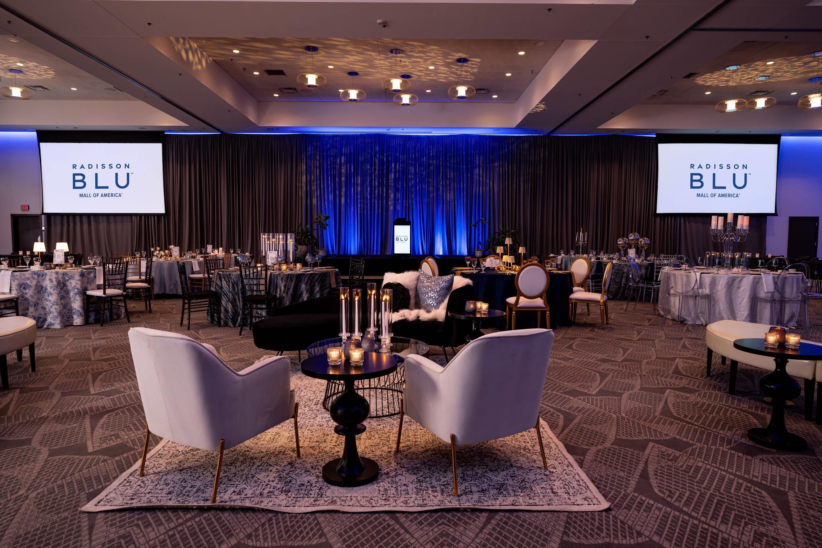 A conference room with a stage, tables, chairs, and a large screen displaying the Radisson Blu logo.