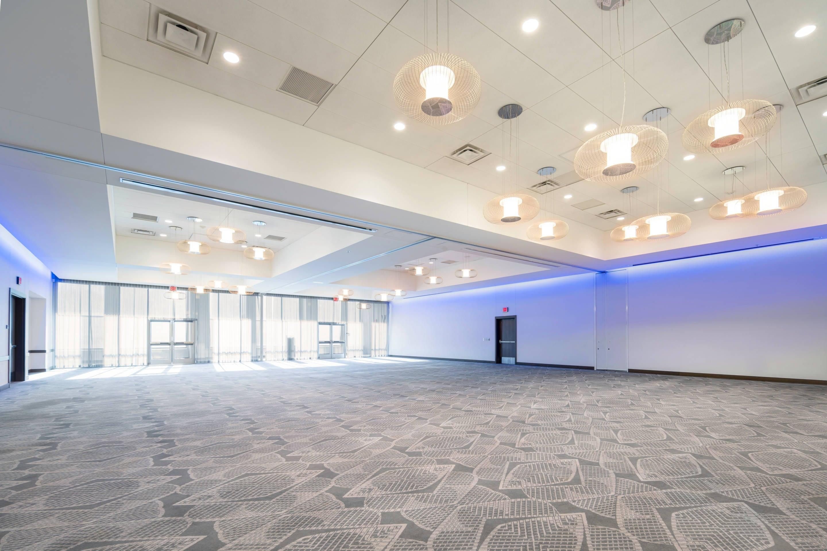 A spacious hotel lobby with patterned carpet, multiple doors, and hanging pendant lights.