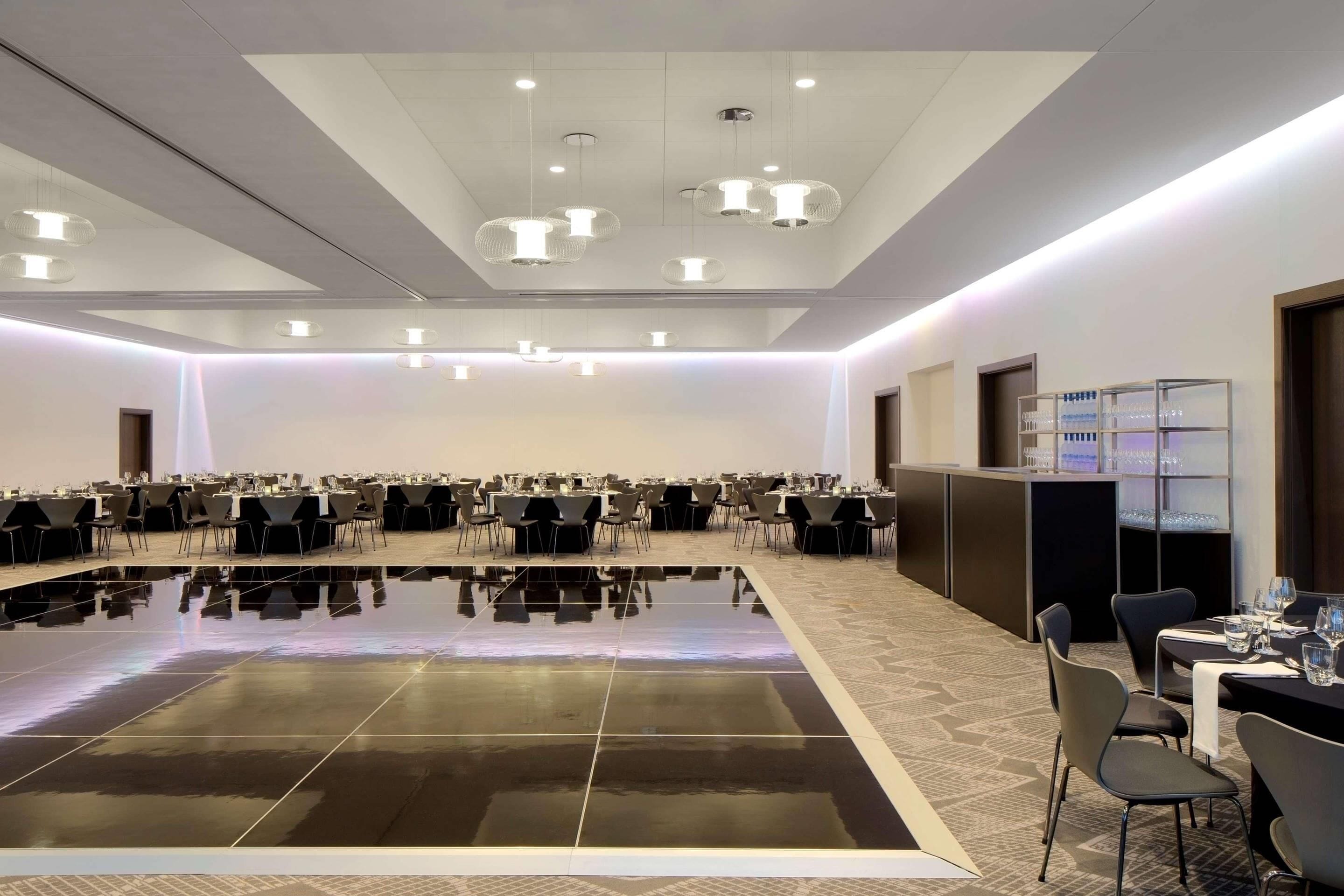 A conference room with a polished floor, tables, chairs, and a bar area with glassware.