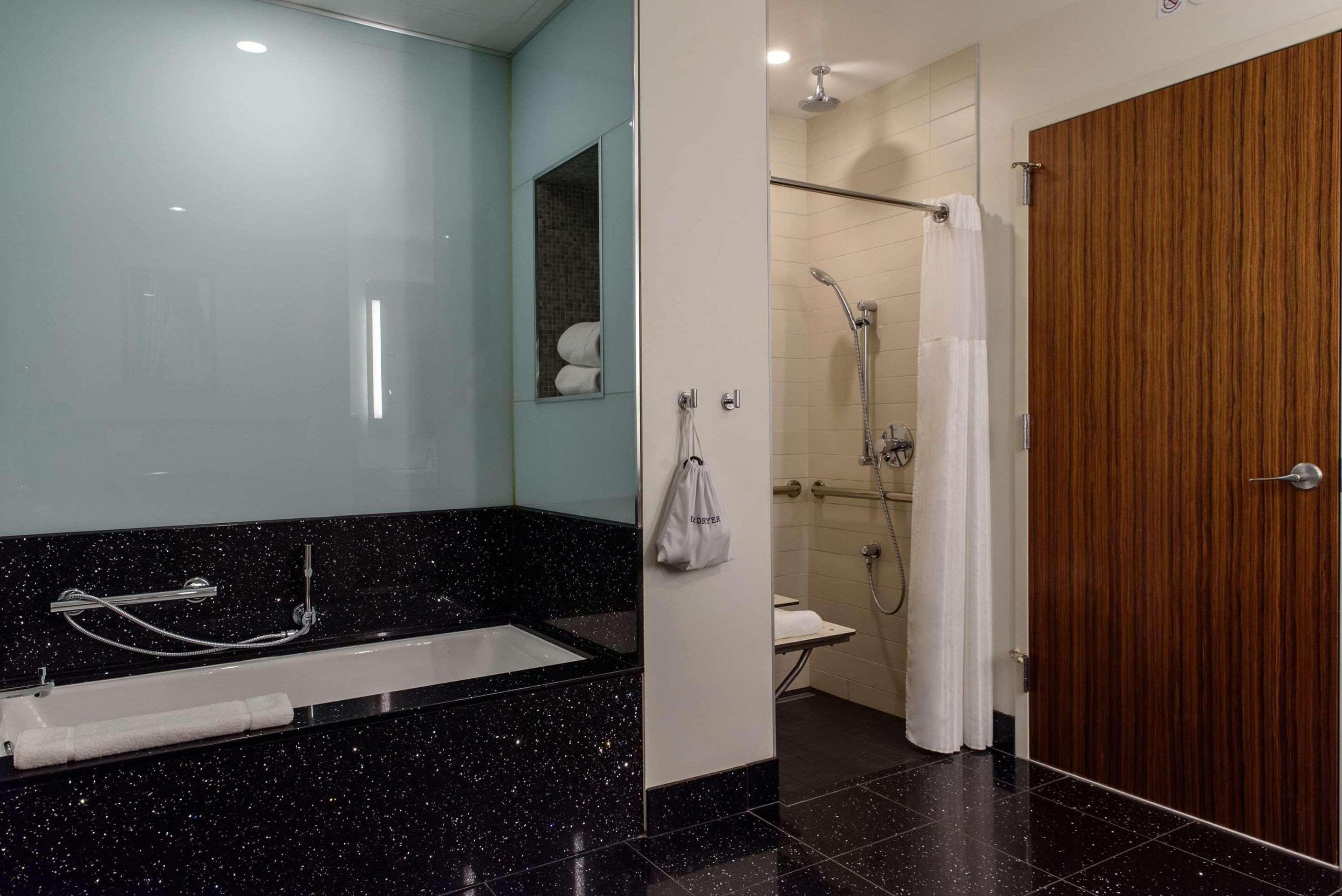A modern bathroom with a black speckled countertop, a shower area, and a wooden door.