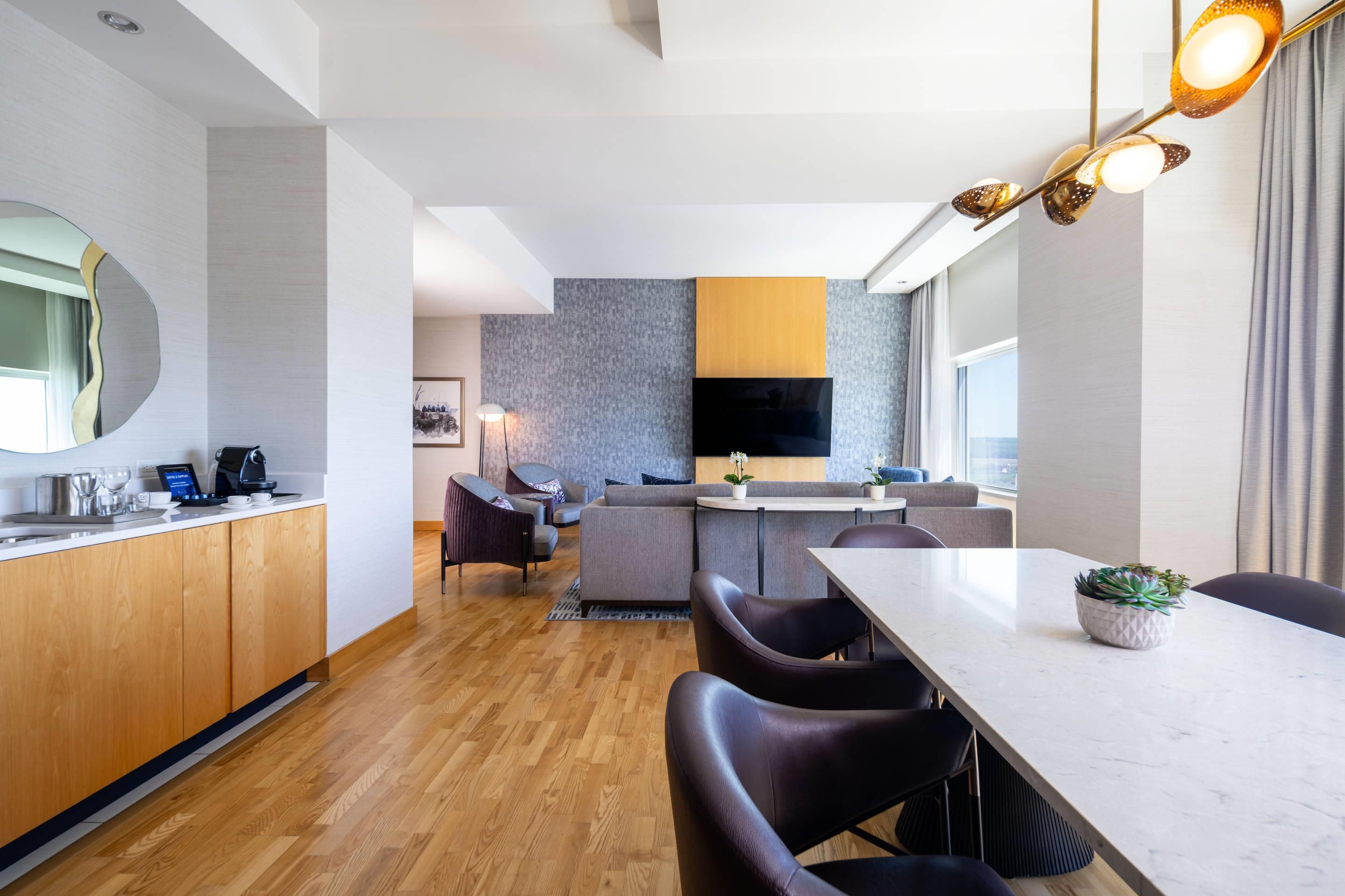 A modern hotel room with a kitchen, dining area, and a living space.