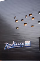 En byggnadsfasad med en modern design, som kännetecknas av en rad jämnt fördelade rektangulära fönster och en framträdande, upplyst skylt med namnet "Radisson Blu".
