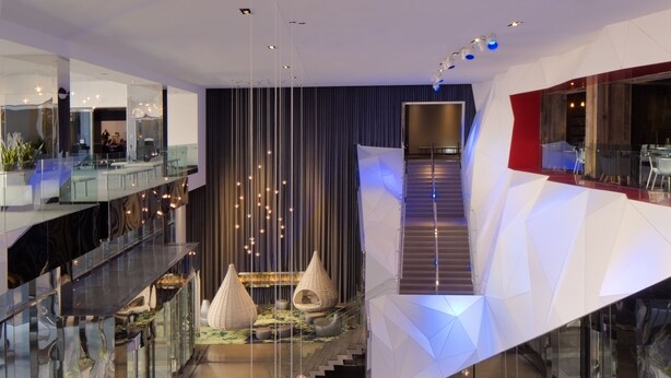 A modern hotel lobby with a central staircase, seating areas, and a reception desk.
