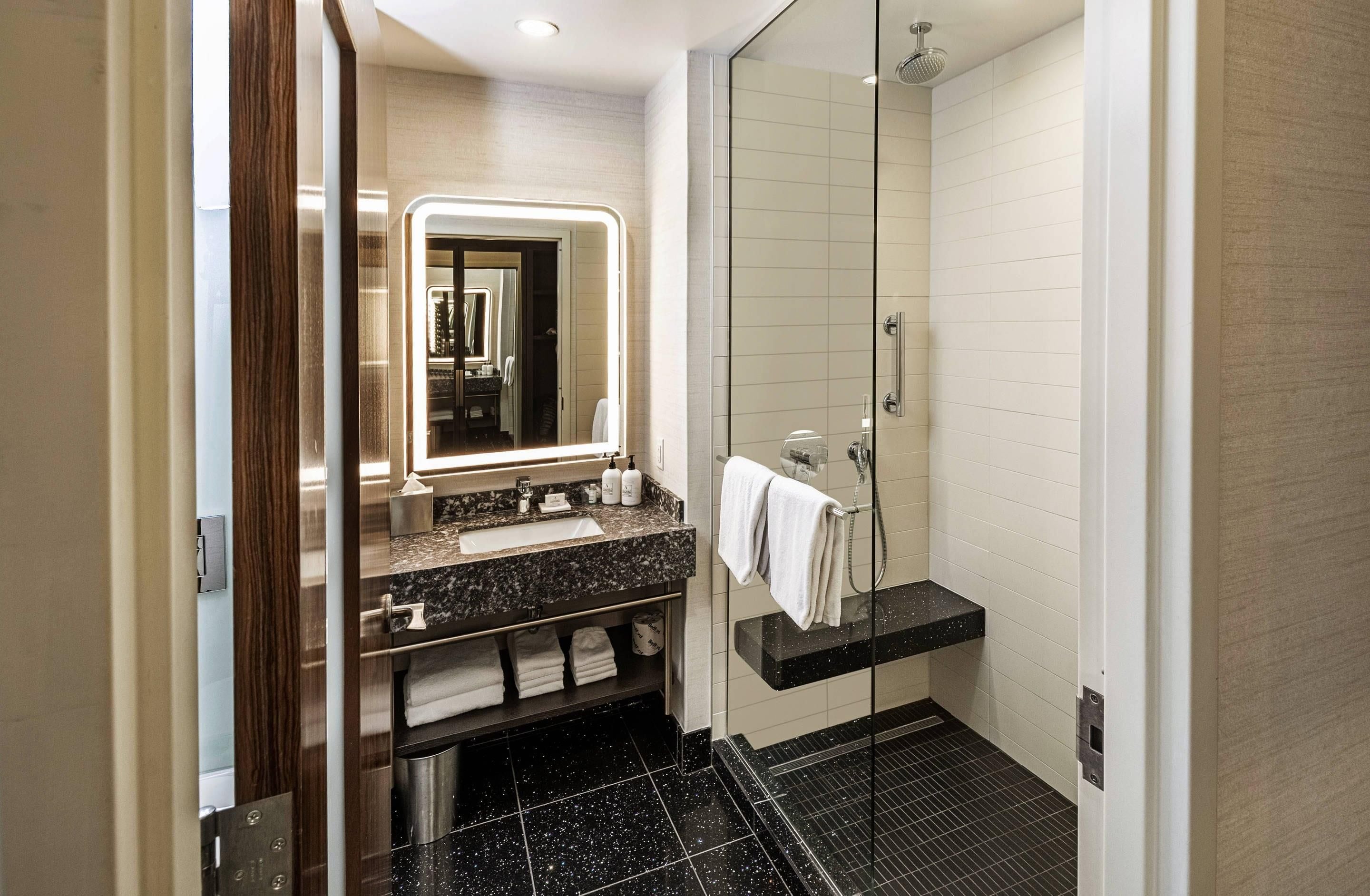 A modern bathroom with a marble sink, a glass shower enclosure, and a vanity with a mirror.