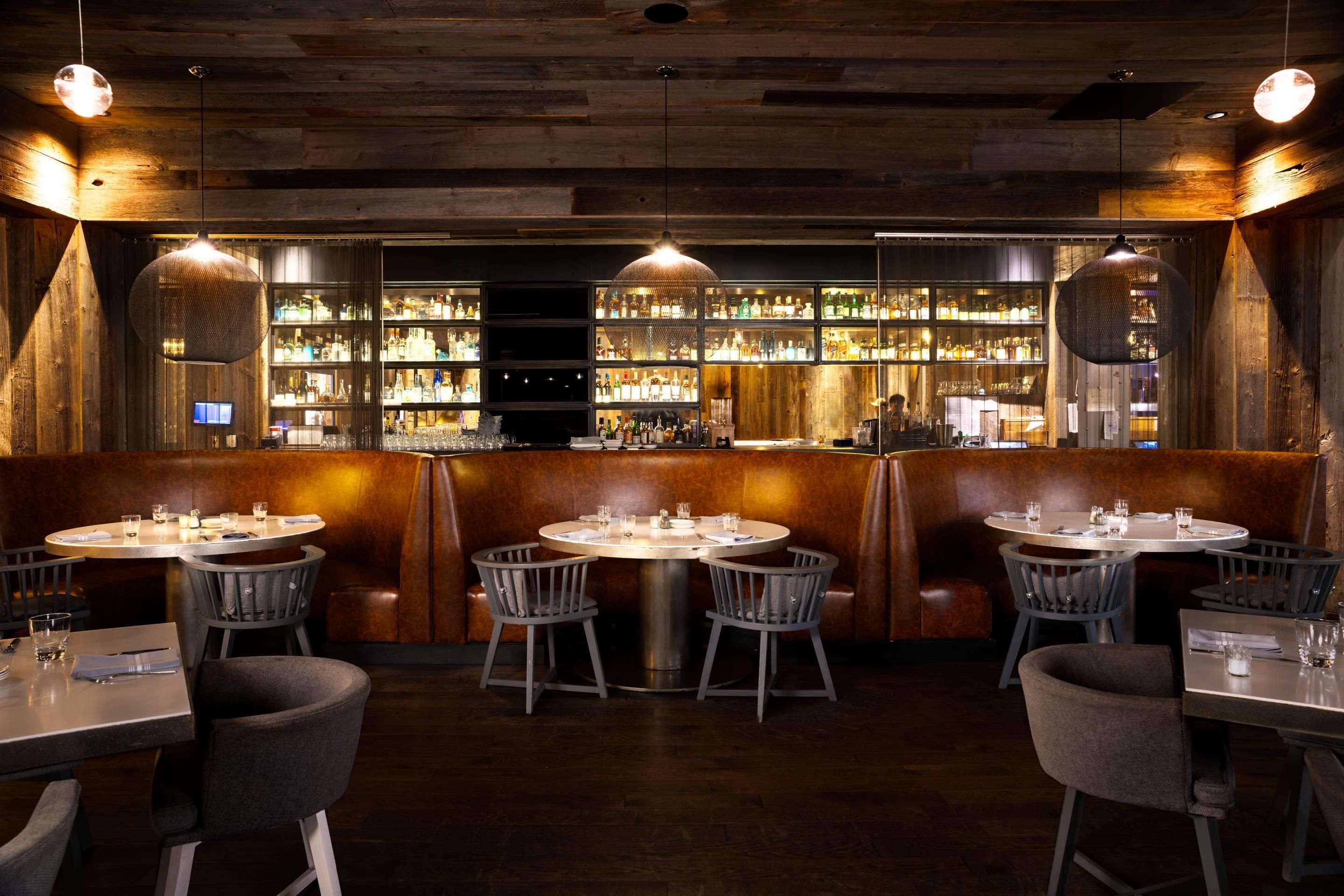 A restaurant with round tables, booths, and a bar area with shelves of bottles.