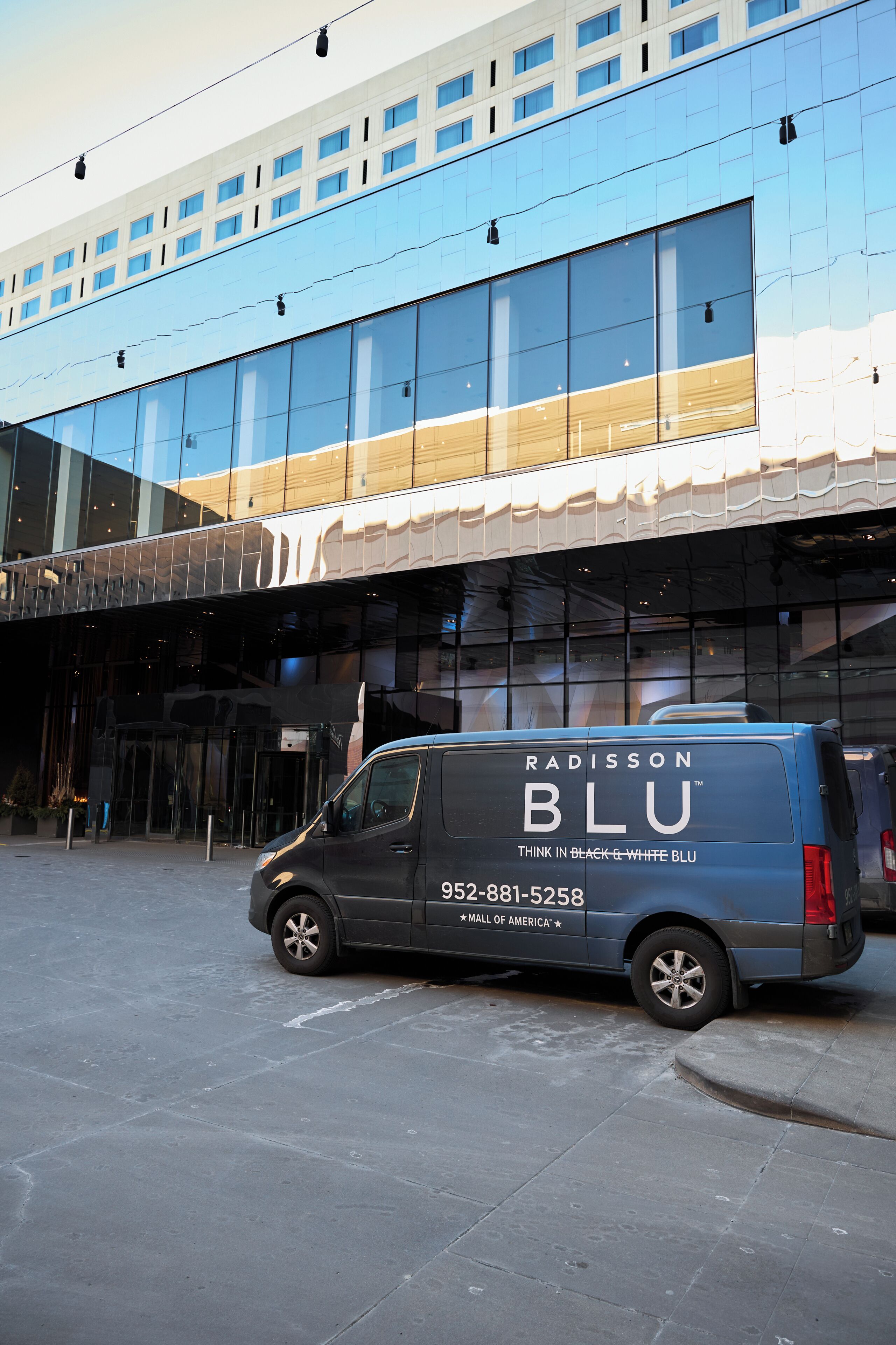 A modern building with a glass facade and a blue van parked in front.